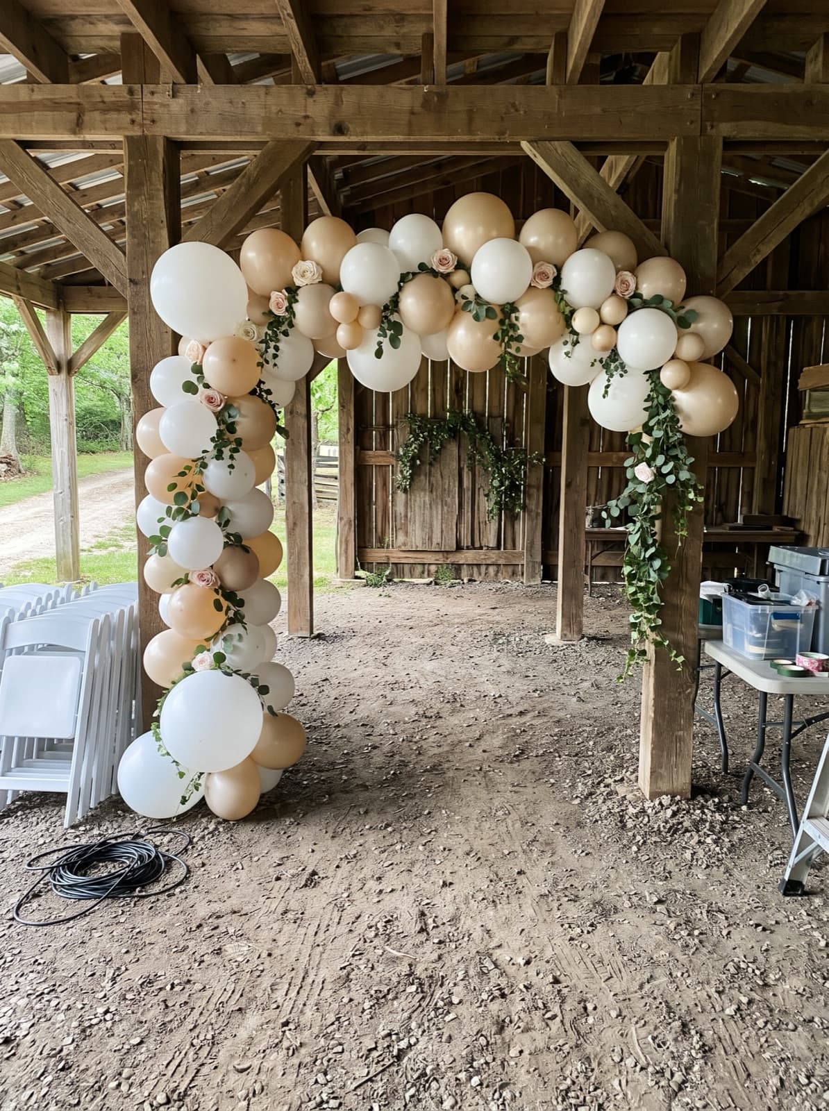Floral balloon arch with greenery inside an open-sided barn