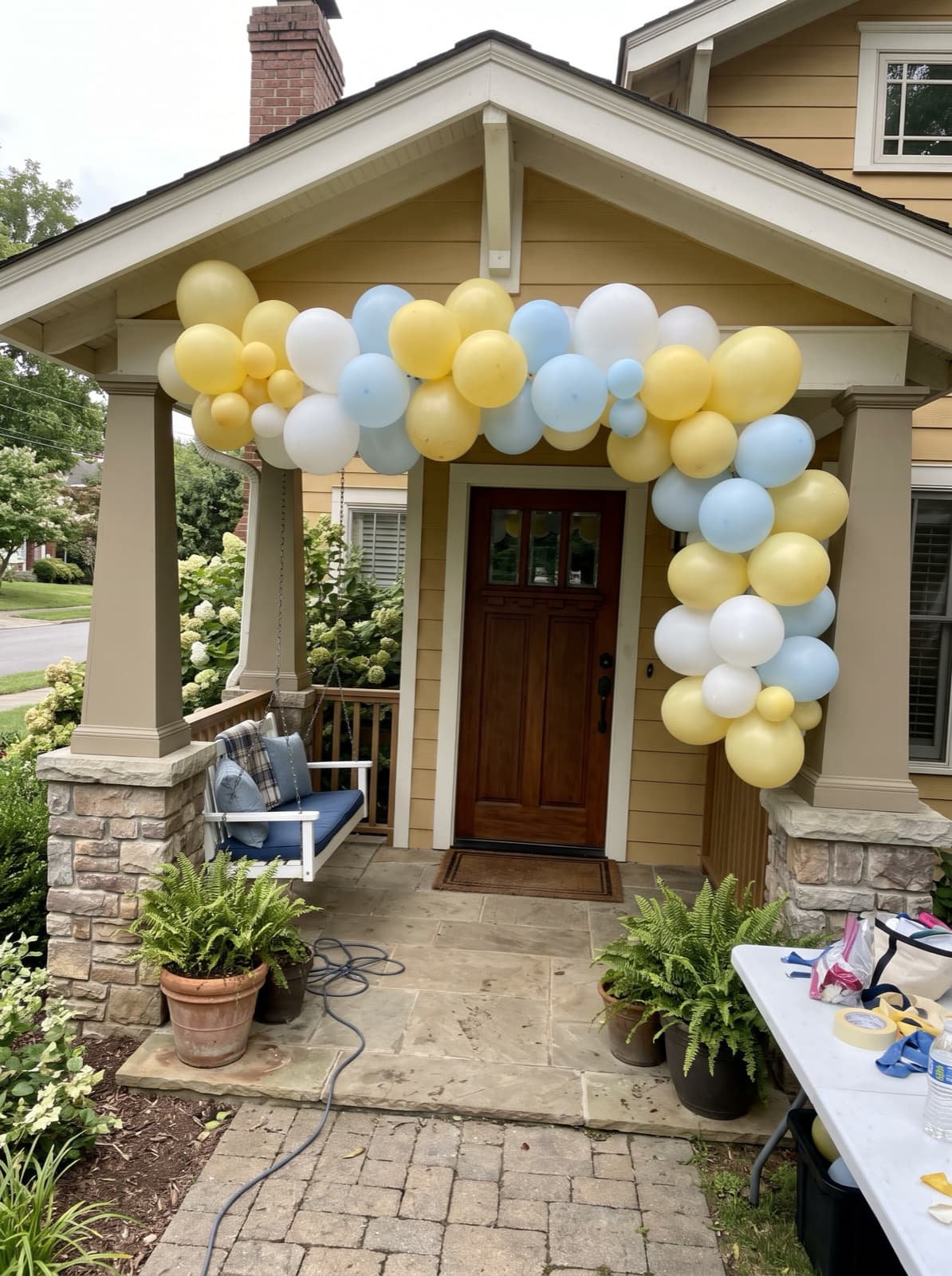Balloon arch over a bungalow front door in butter yellow, white and pale blue