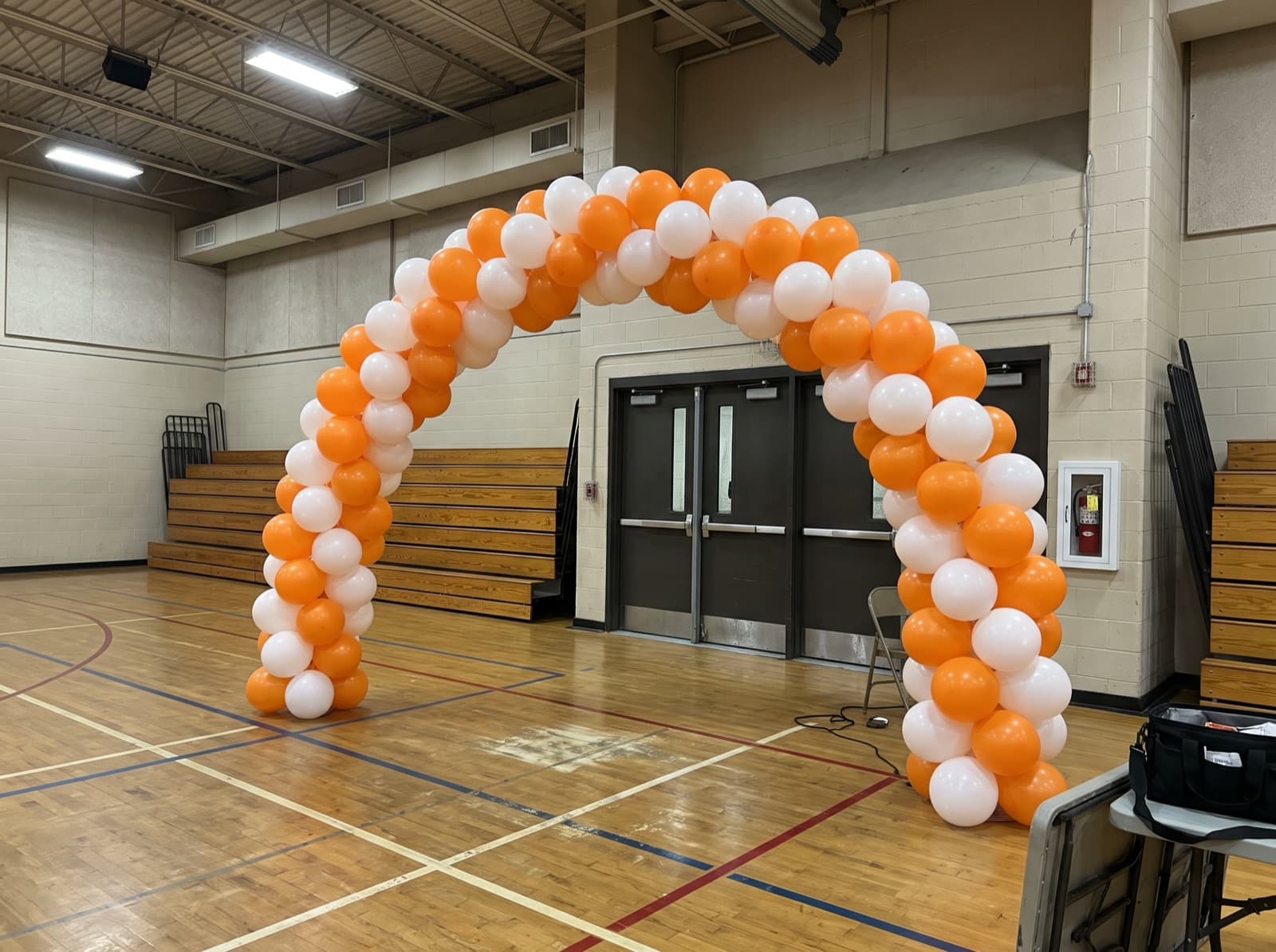 Spiral balloon arch in orange and white over a gym entrance