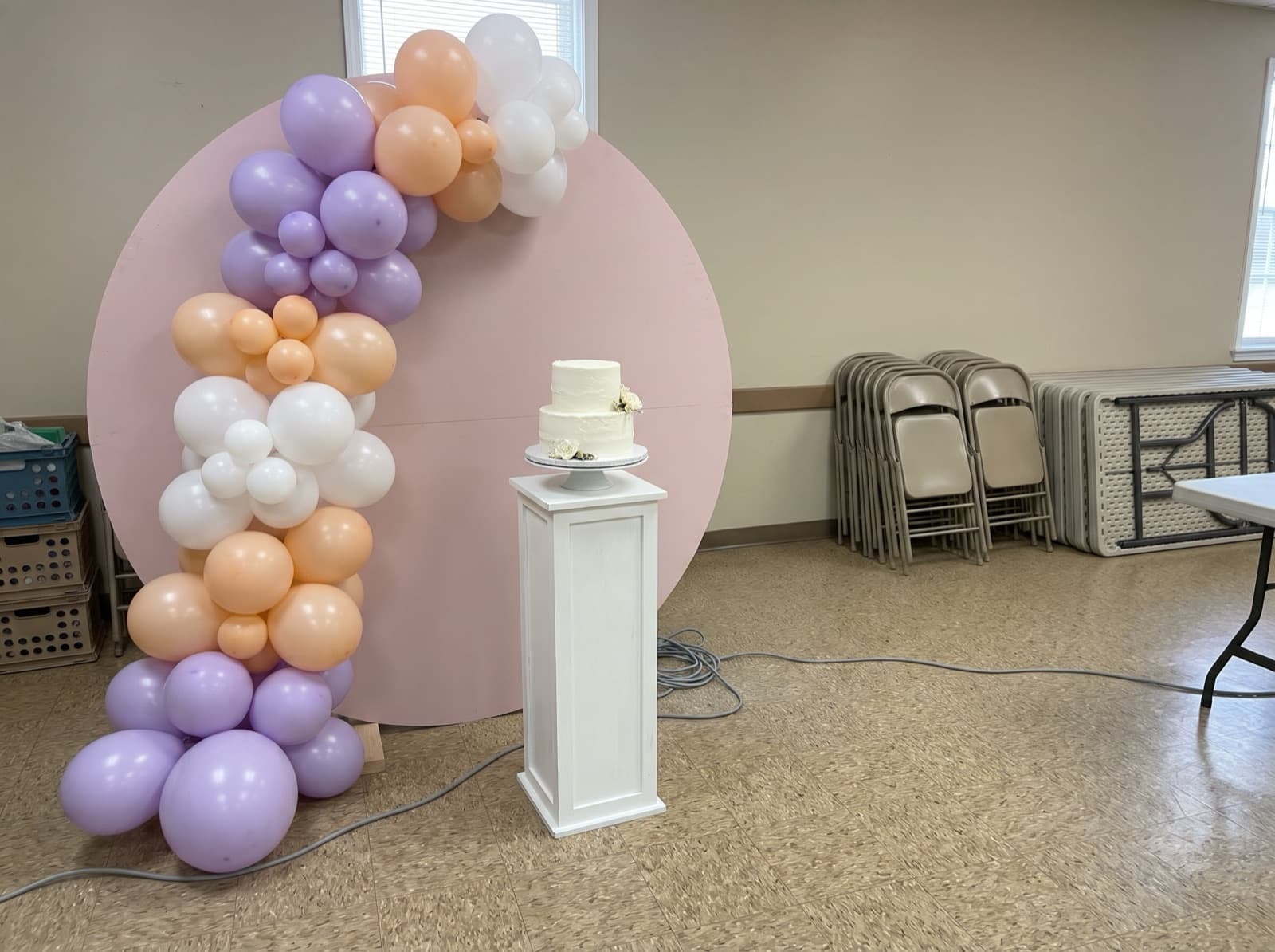 Round backdrop with a lavender, peach and white organic balloon garland and a cake on a pedestal
