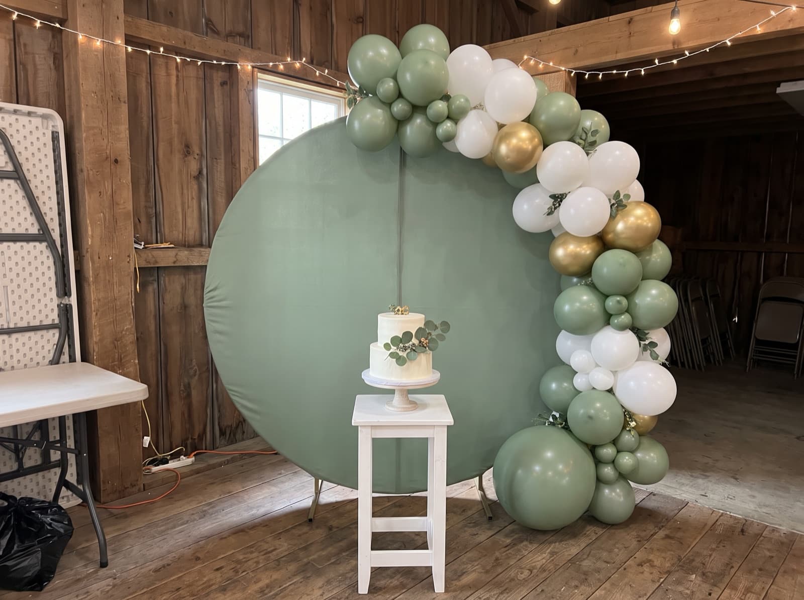 Round sage backdrop with a white and gold balloon garland
