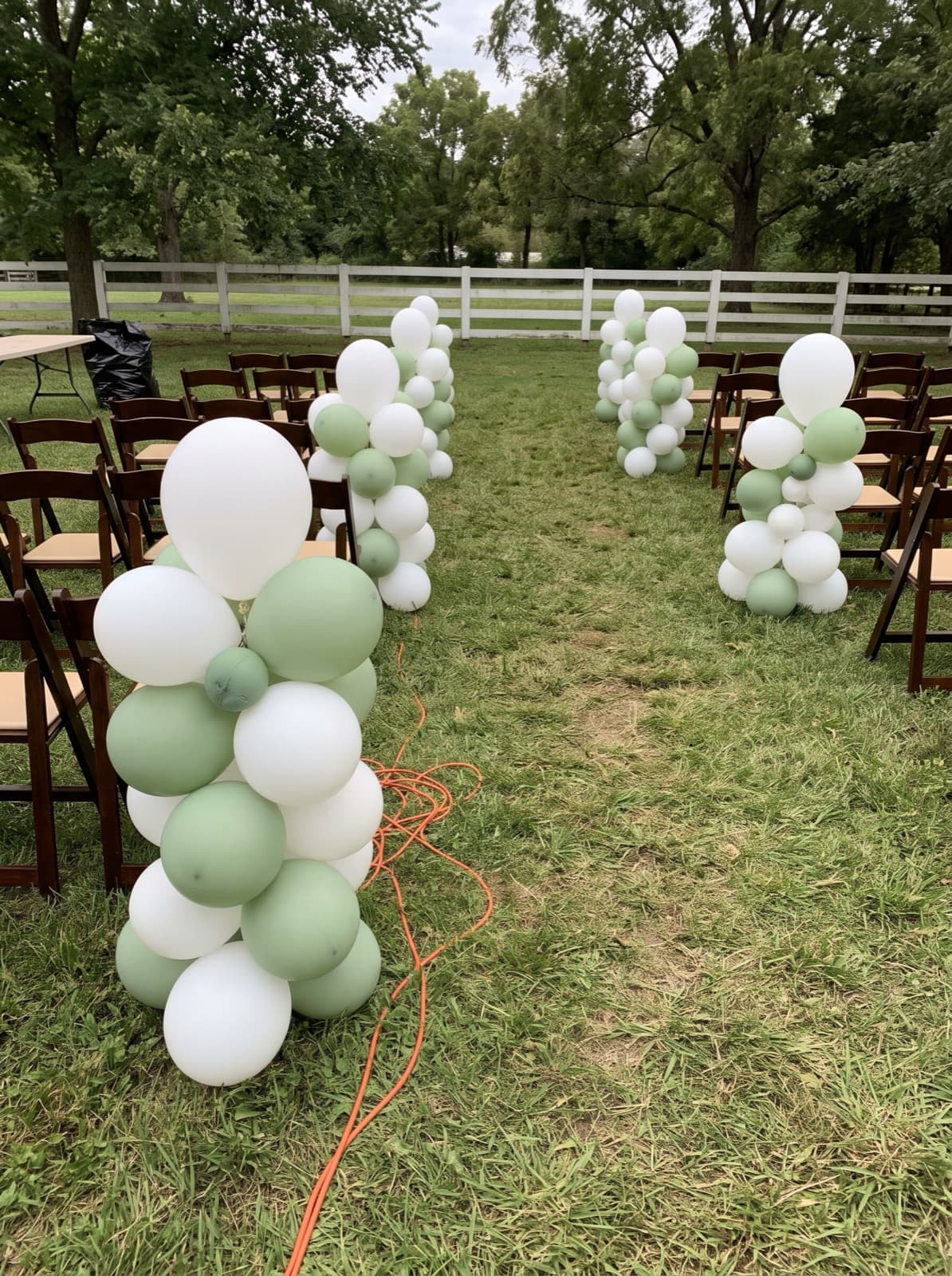 Organic balloon columns lining an outdoor ceremony aisle