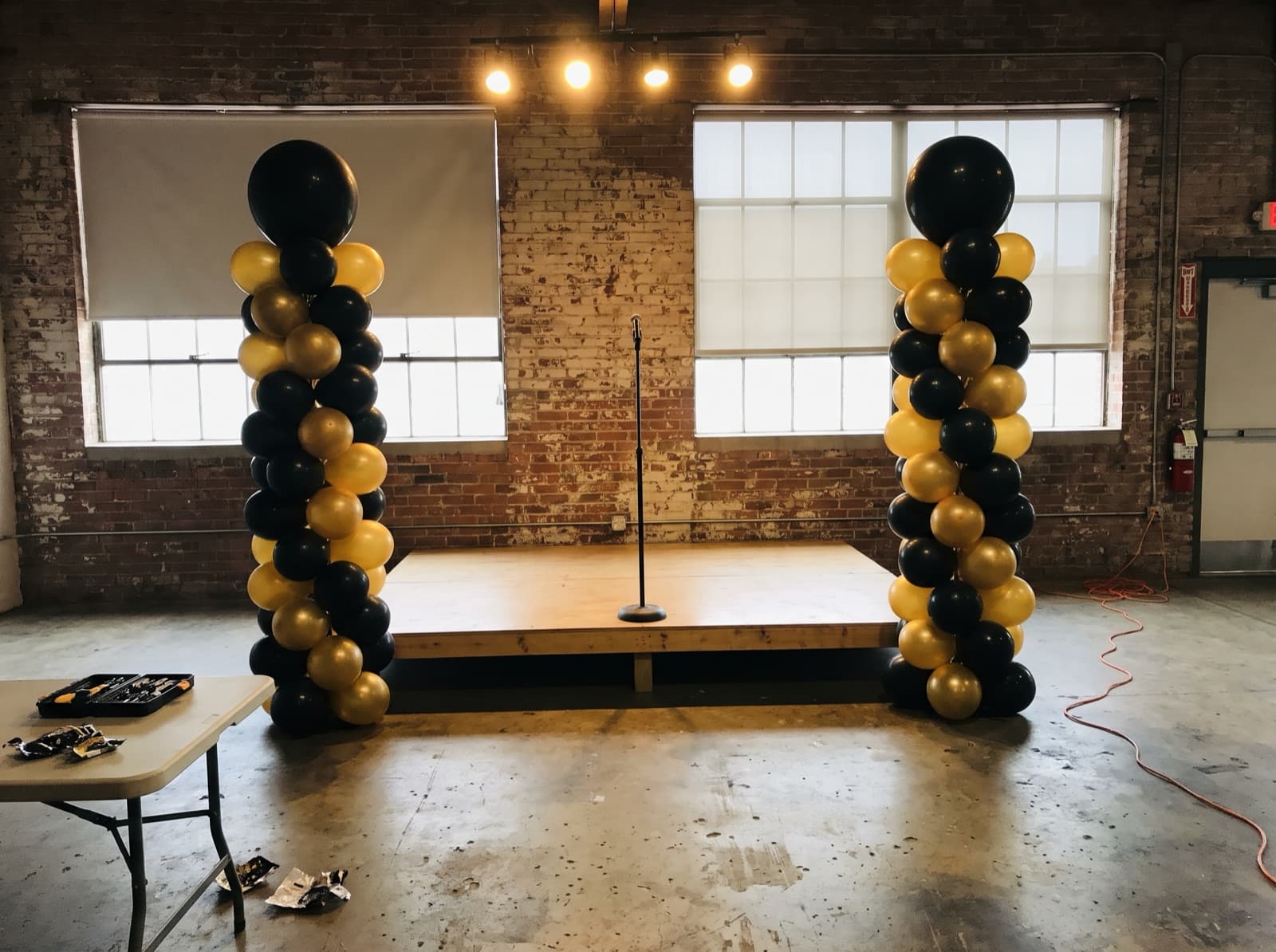 Tall black and gold balloon columns beside a small stage
