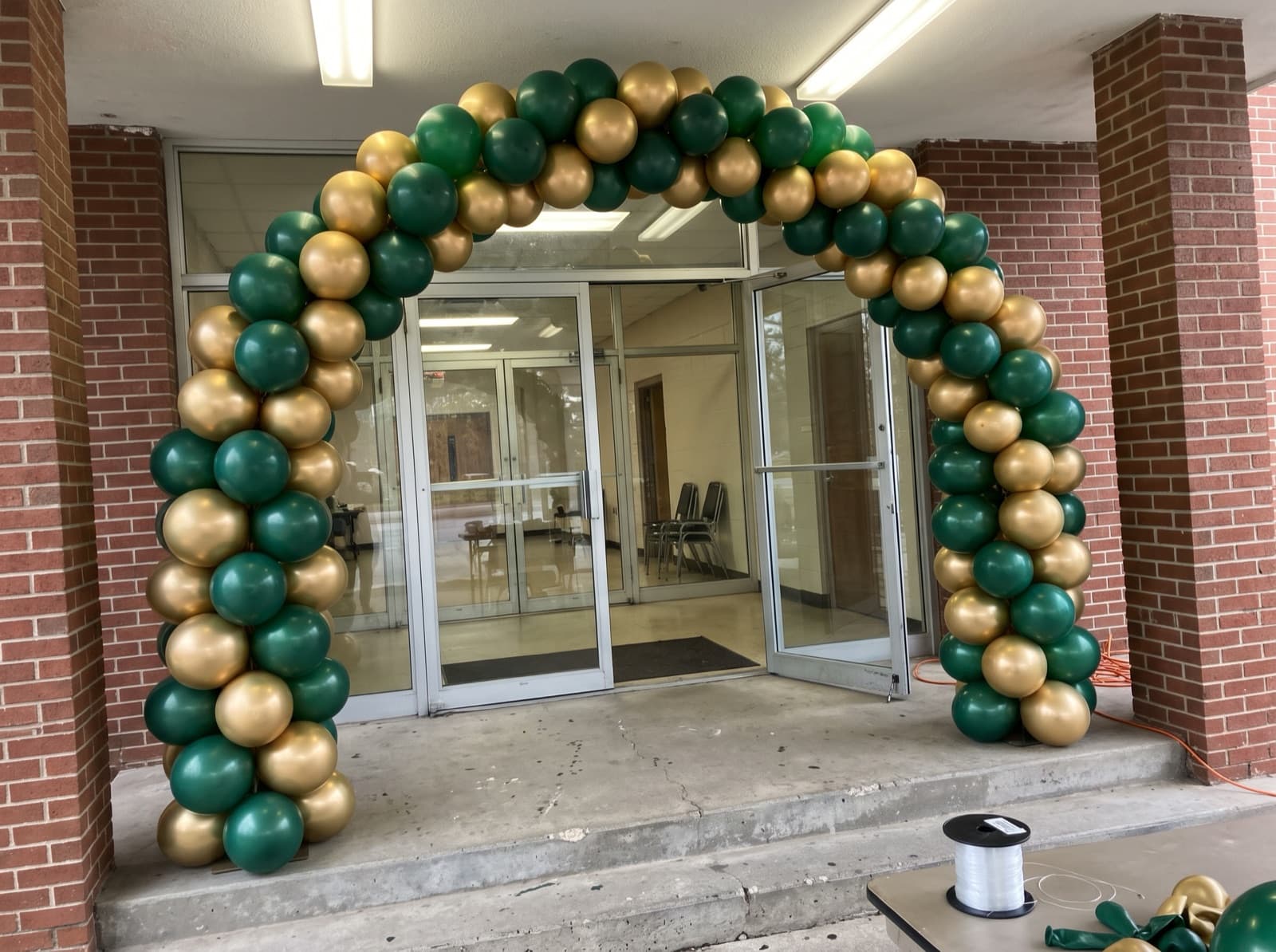 Balloon columns joined by a green and gold arch