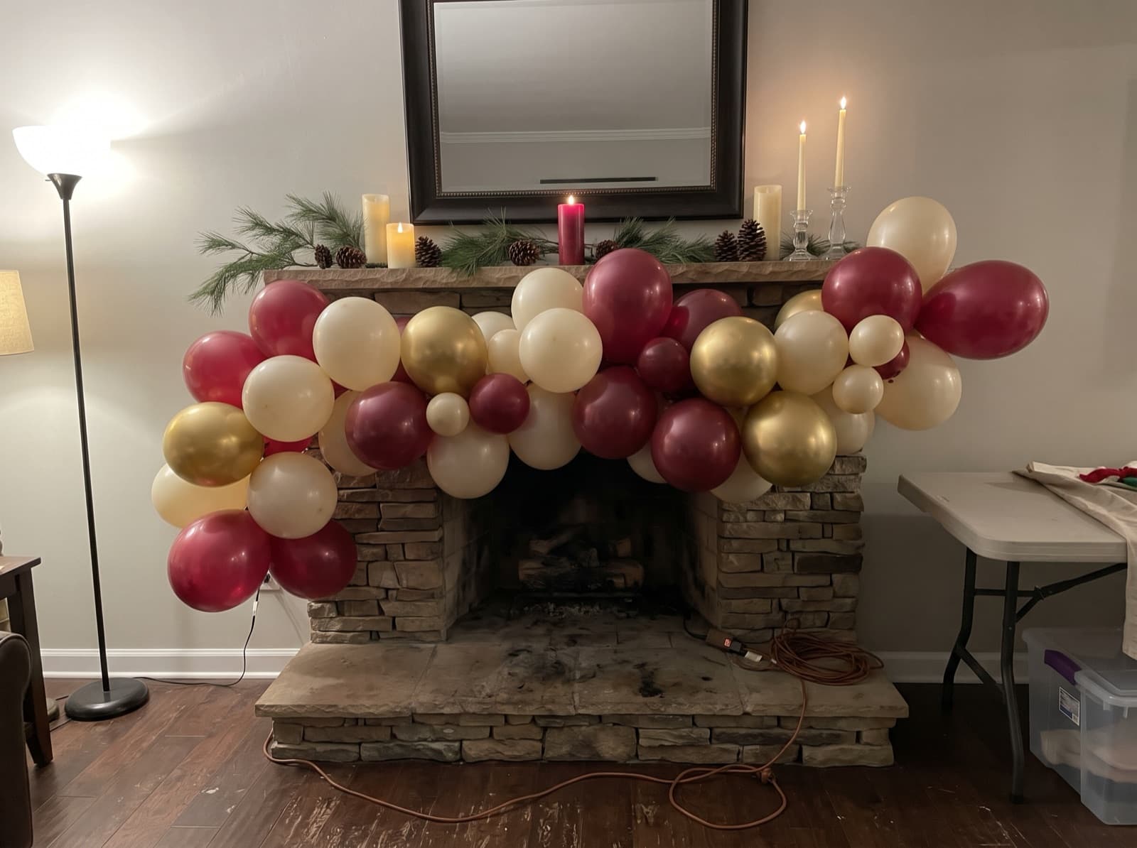Deep red, cream and gold balloon garland along a stone fireplace mantel